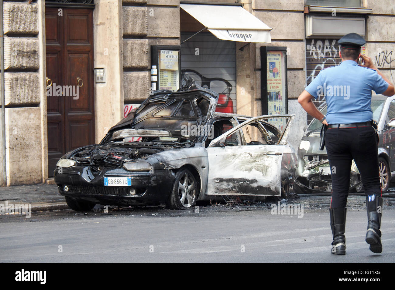 Un policier s'occupant d'une voiture brûlée dans une rue de Rome. Banque D'Images