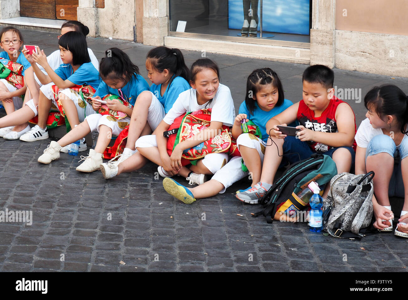 Les enfants chinois assis dans une rangée sur le trottoir.cobblestone Banque D'Images