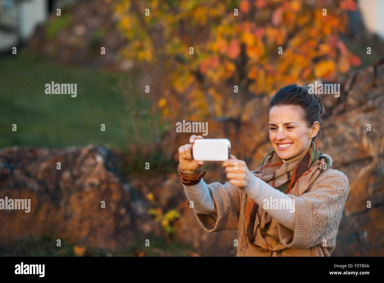 Smiling young brunette woman taking photo avec un téléphone mobile tout en vous relaxant dans un beau soir in autumn park Banque D'Images