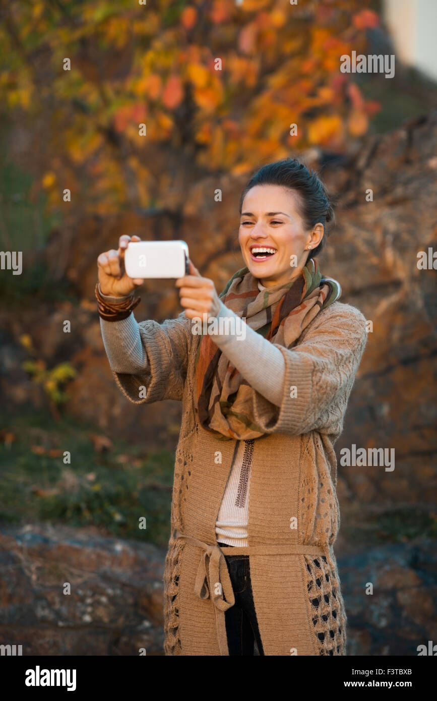 Moderne heureux brown-haired woman taking photo de belle vue avec téléphone cellulaire à l'automne à l'extérieur en soirée Banque D'Images