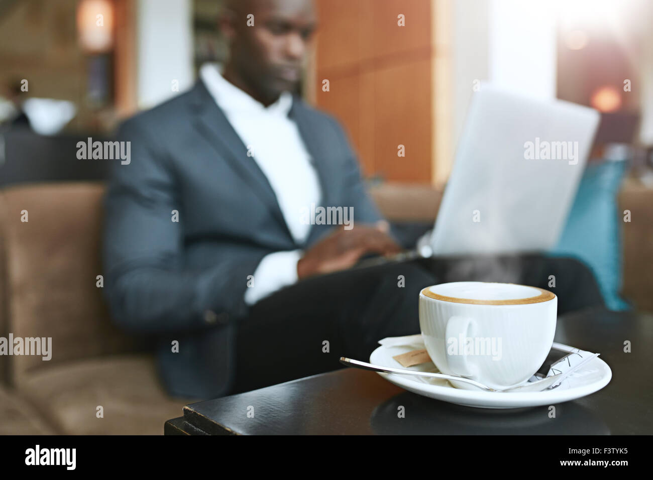 Jolie tasse de café chaud sur la table avec un businessman sitting in background working on laptop at hall de l'hôtel. Banque D'Images
