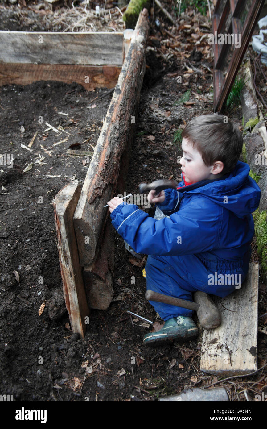 Petit garçon en utilisant un marteau pour frapper clou dans le cadre en bois de jardin Banque D'Images
