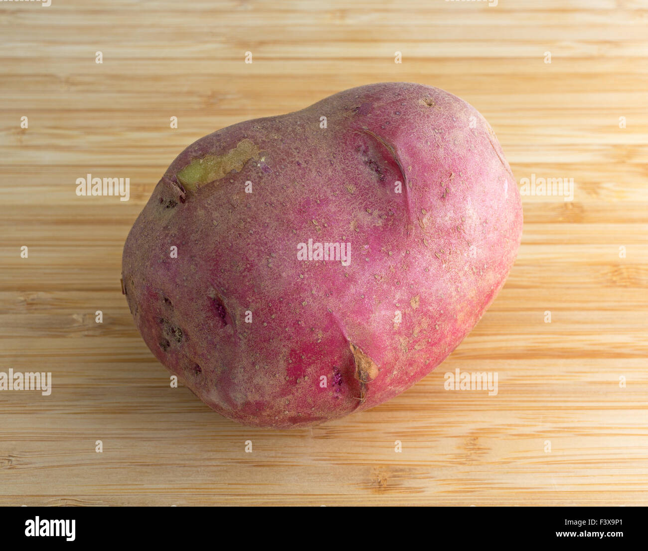 Une culture biologique de pommes de terre rouge sur une planche à découper en bois éclairé par la lumière naturelle. Banque D'Images