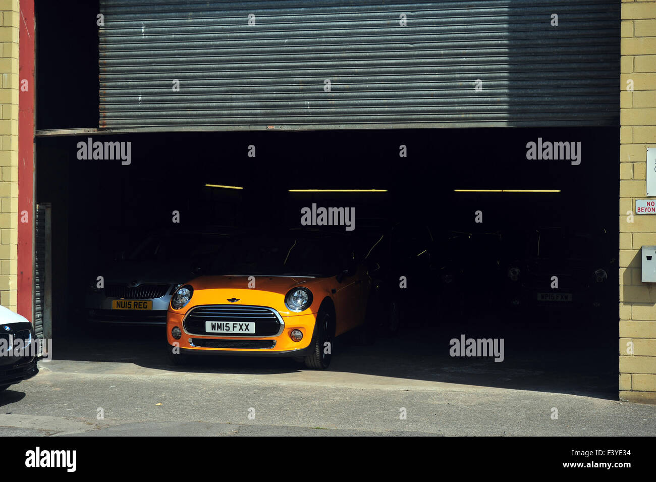 Le capot d'une voiture BMW Mini orange moderne dépasse de sous une porte de garage. Banque D'Images