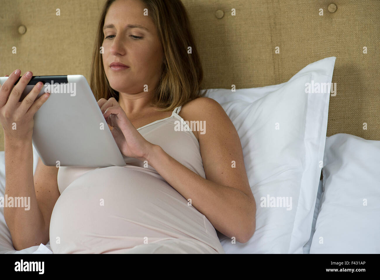 Pregnant woman Lying in Bed using digital tablet Banque D'Images