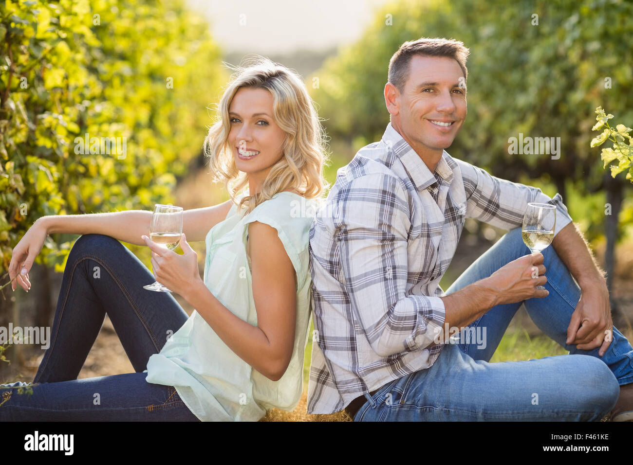 Portrait of smiling couple assis dos à dos avec verre à côté de grapevine Banque D'Images Portrait of smiling couple assis dos à dos avec verre à côté de grapevine Banque D'Images