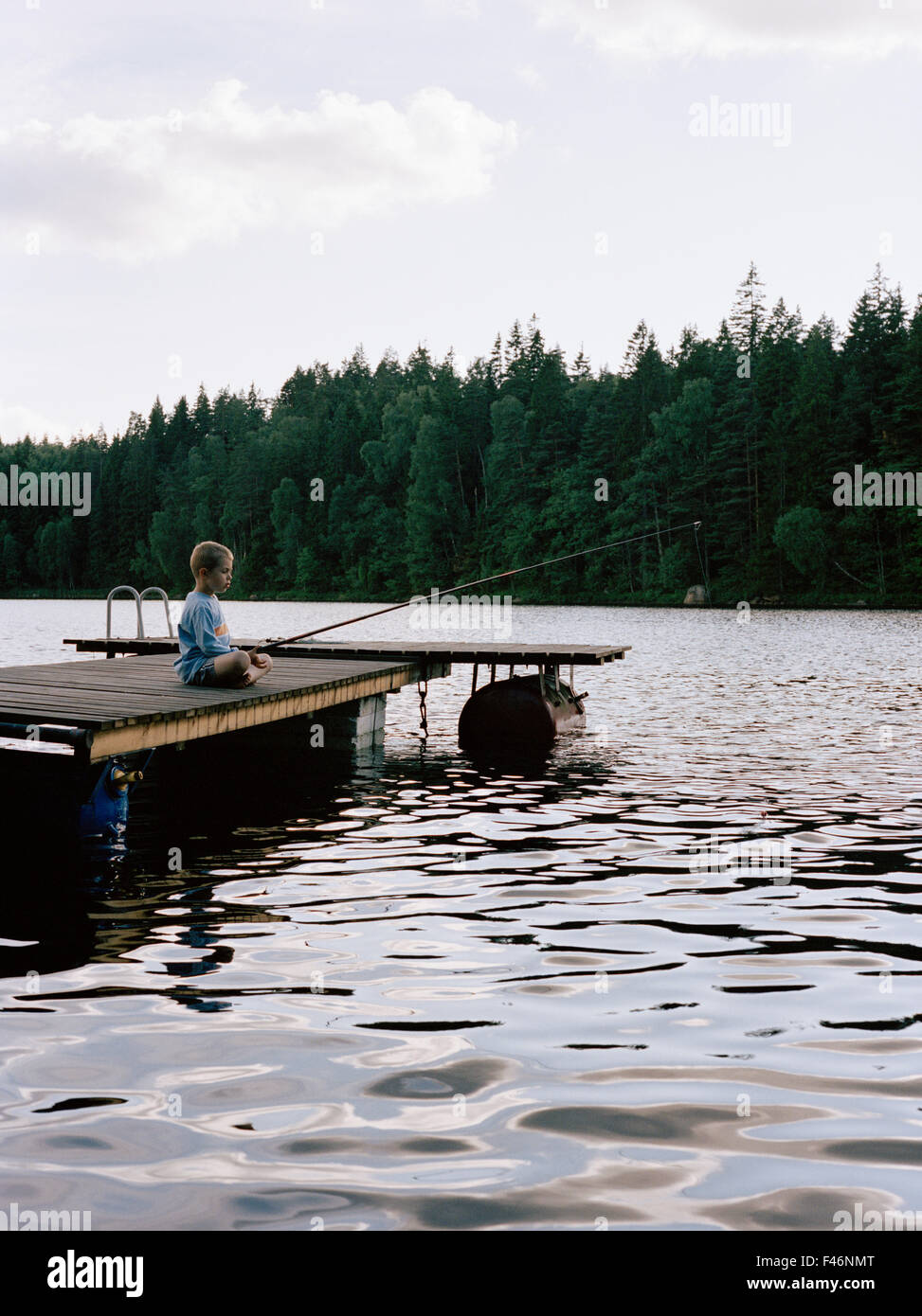 Un garçon assis sur une jetée de pêche, la Suède. Banque D'Images
