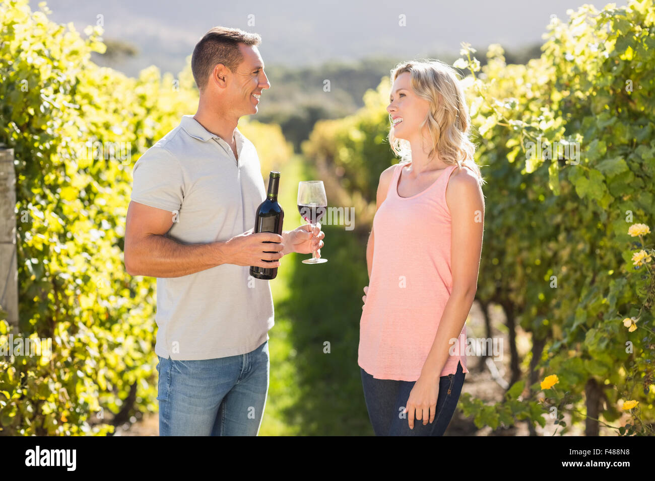 Smiling couple holding wine et debout à côté de grapevine Banque D'Images Smiling couple holding wine et debout à côté de grapevine Banque D'Images