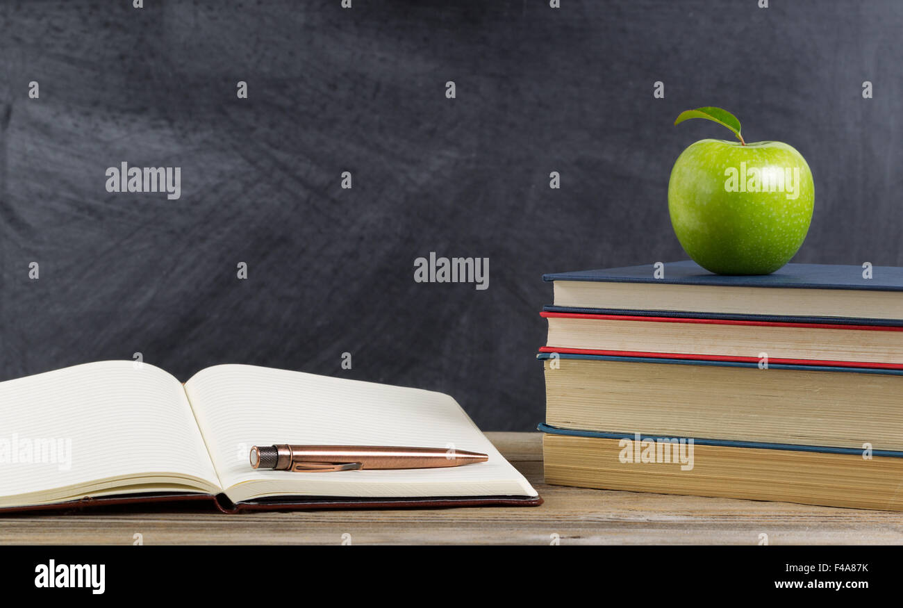 Bureau rustique de l'étudiant, vue en gros, avec des livres, du papier et un stylo ainsi qu'un green apple en avant du tableau. Banque D'Images
