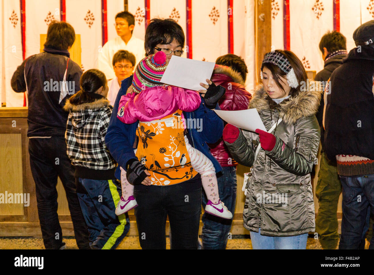 Minuit, le jour de l'an japonais au sanctuaire. Jeune couple, l'homme porte un porte-bébé avec bébé. Il épouse et lecture omikuji papers fortune. Banque D'Images