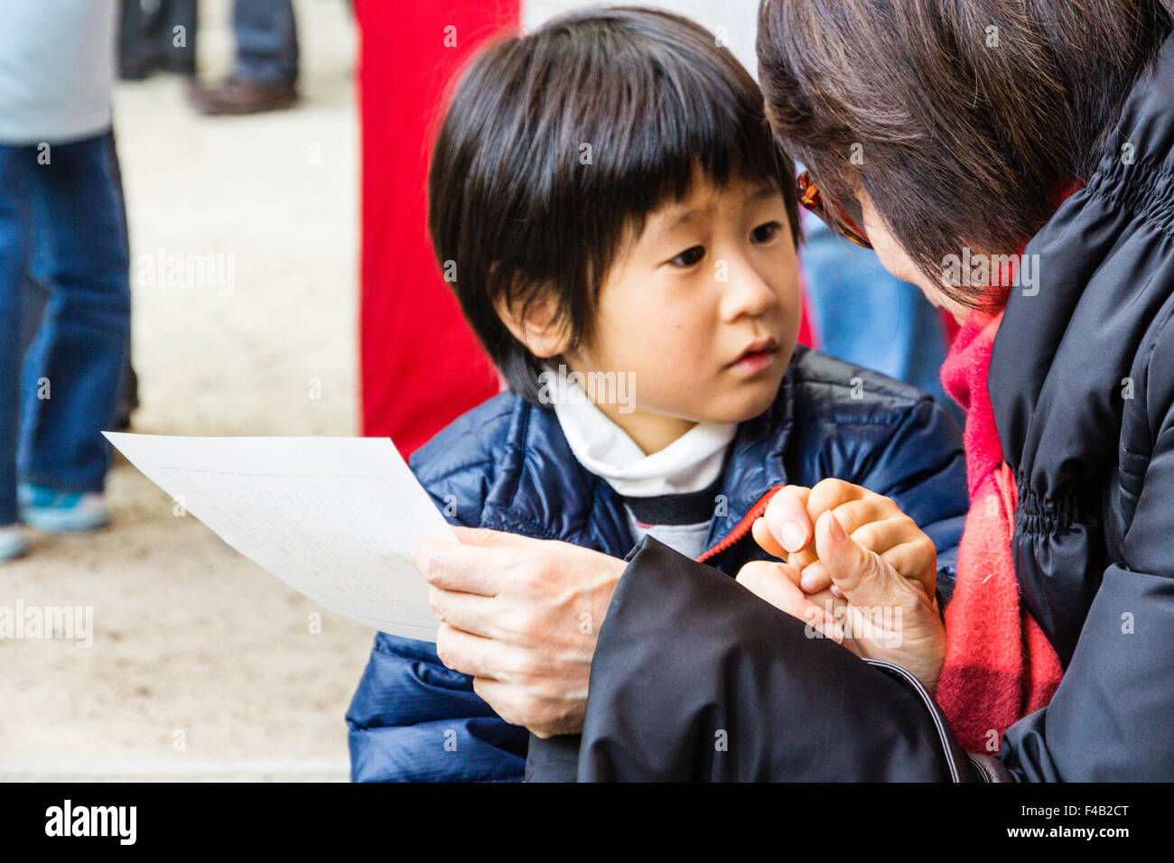 Culte japonais. Mère détient main de petit enfant, garçon, 5-6 ans, qu'elle lit un omikuji, fortune papier. Très anxieux expression sur visage du garçon. Banque D'Images
