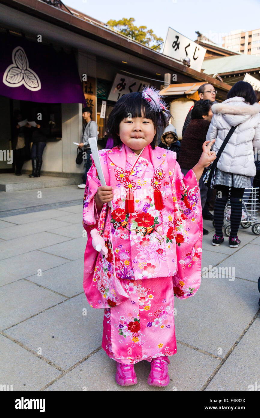 Le Japon, Nishinomiya culte, nouvelle année. Enfant, fille, 4-5 ans l'article posant pour viewer en kimono rose et rouge et en donnant deux doigt geste de paix. Banque D'Images