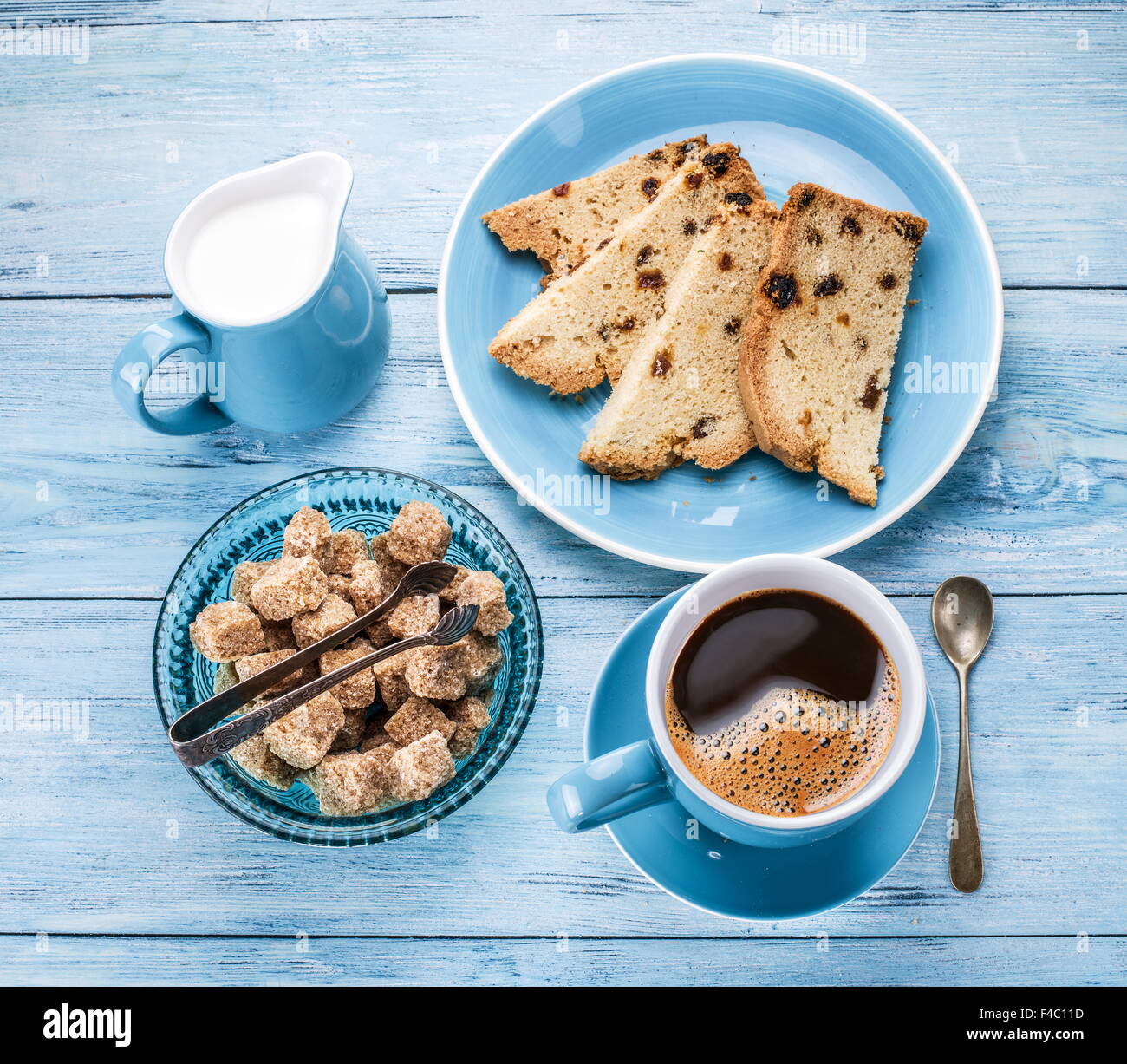 Tasse de café, de lait, de sucre de canne glaçons et fruits-gâteau sur une vieille table en bois bleu. Banque D'Images