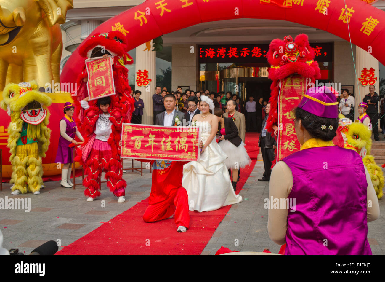 Yantai, Shandong, Chine. Un couple nouvellement marié passez par les mouvements de leur célébration de mariage coloré. Banque D'Images