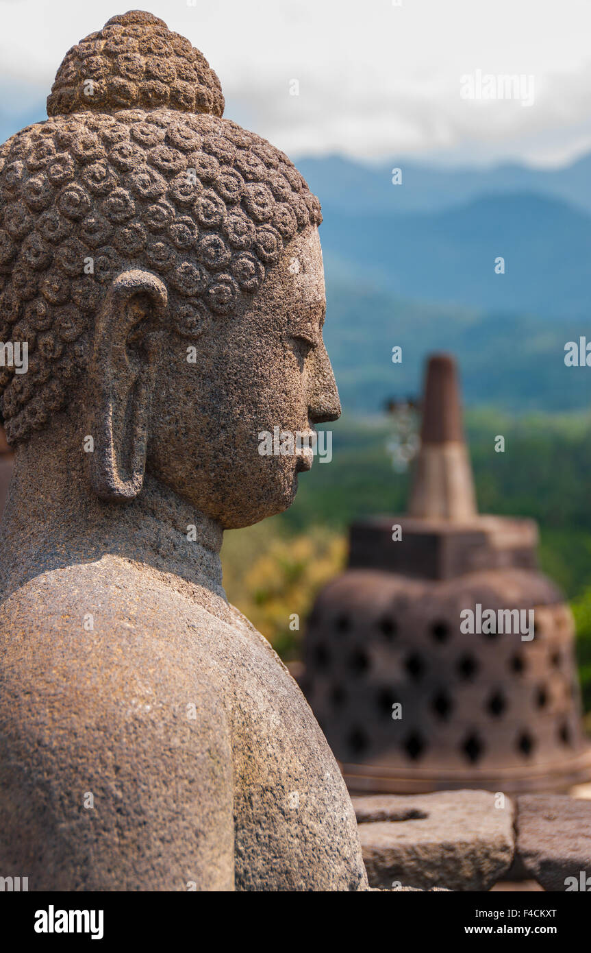 Assis en face de Bouddha en pierre au Stupa de Borobudur Banque D'Images
