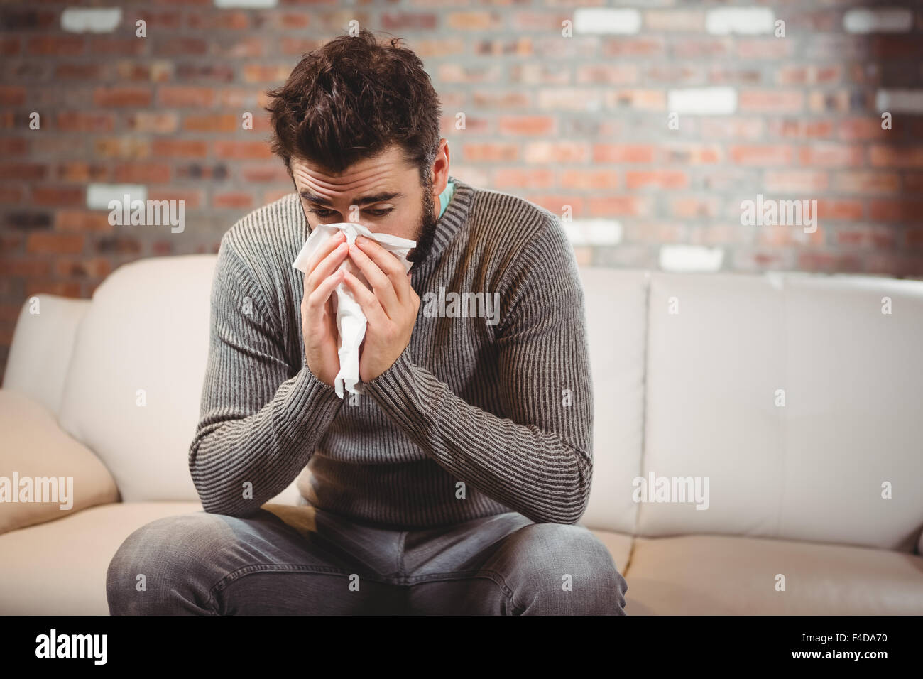 Homme assis sur un canapé et blowing nose Banque D'Images