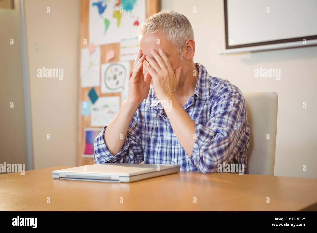 Frustrés businessman with head in hands at desk Banque D'Images