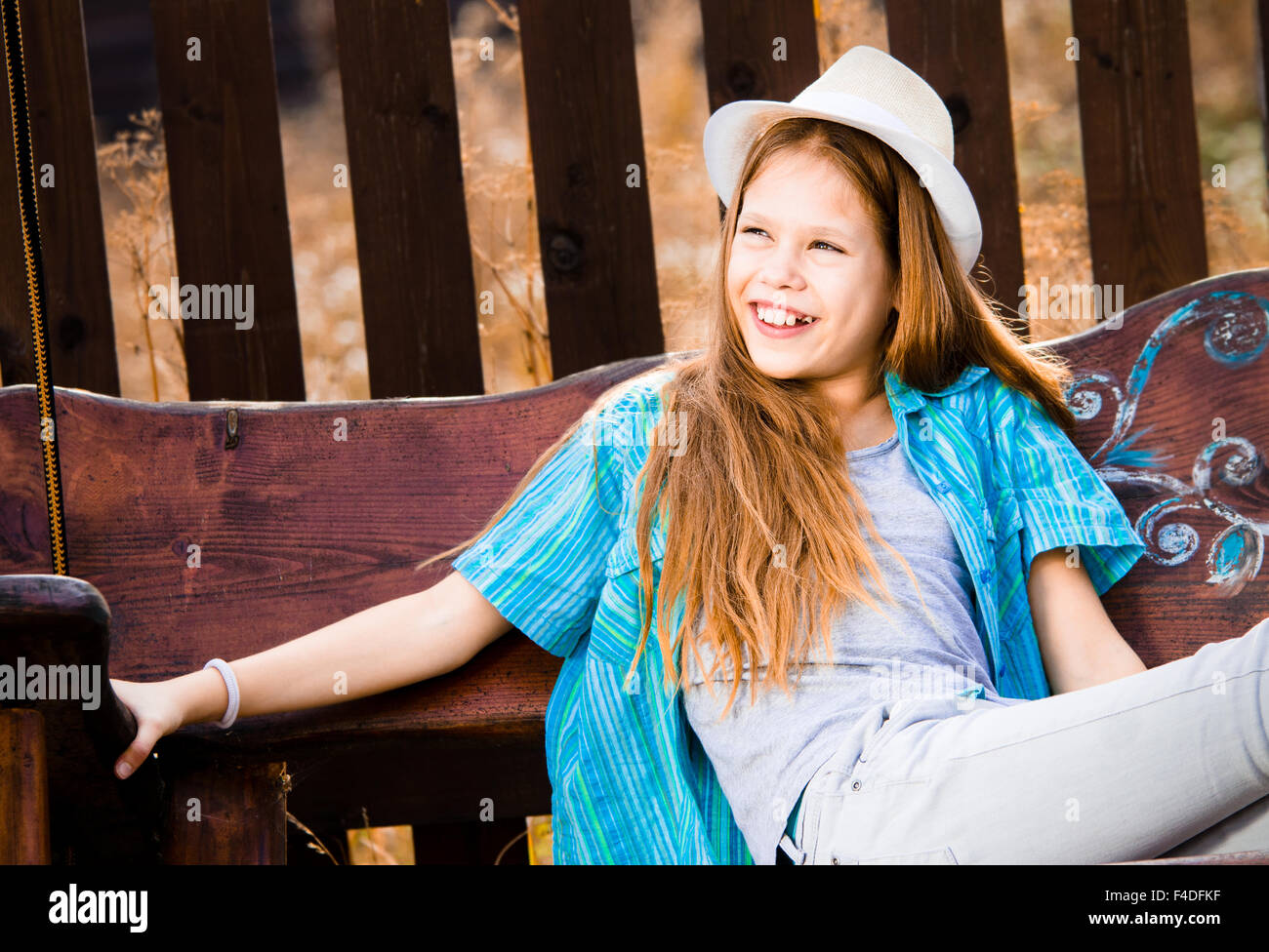 Belle jeune fille de 11 ans, assis sur une balançoire, portant un chapeau blanc. En souriant. Couleurs d'automne. Banque D'Images