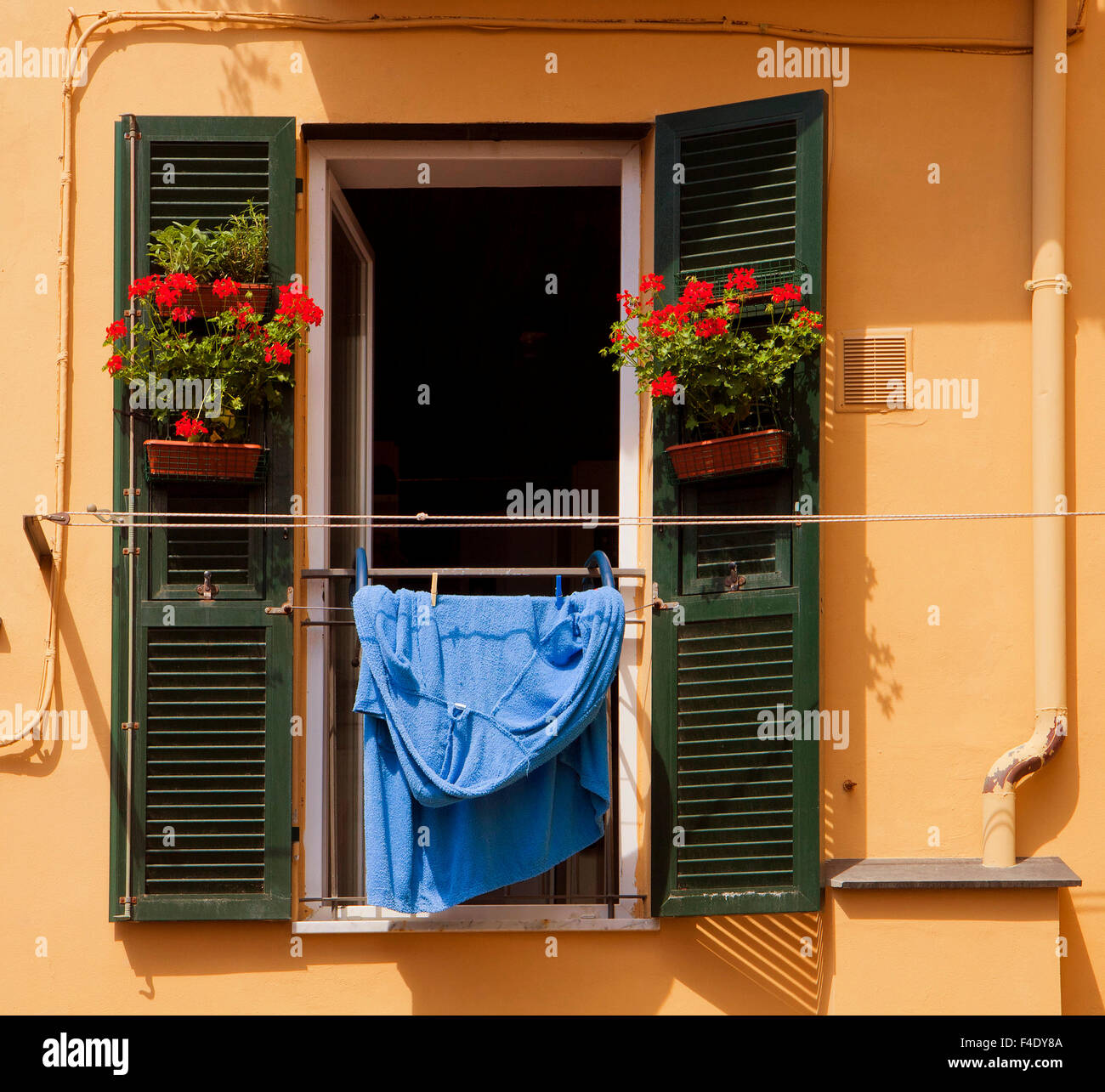 Les couleurs italiennes : fenêtre avec volets ouverts, géranium rouge et bleu de vases suspendus blanchisserie au soleil Banque D'Images