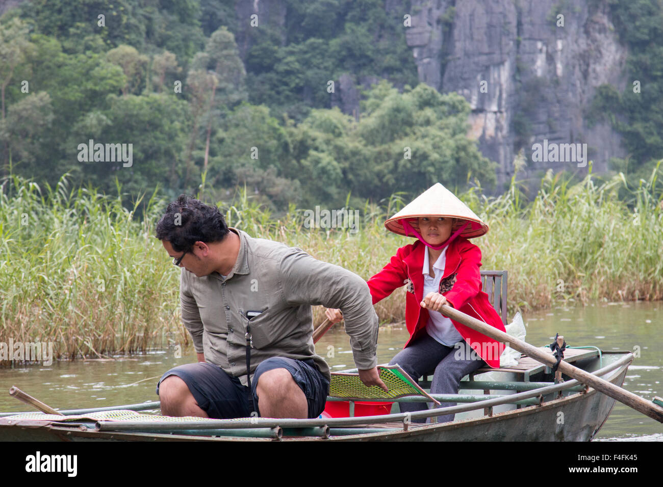 Femme vietnamienne rame le touriste masculin en barque le long de la rivière NGO Dong Tam Coc vers les trois grottes, Ninh Binh, Vietnam Banque D'Images