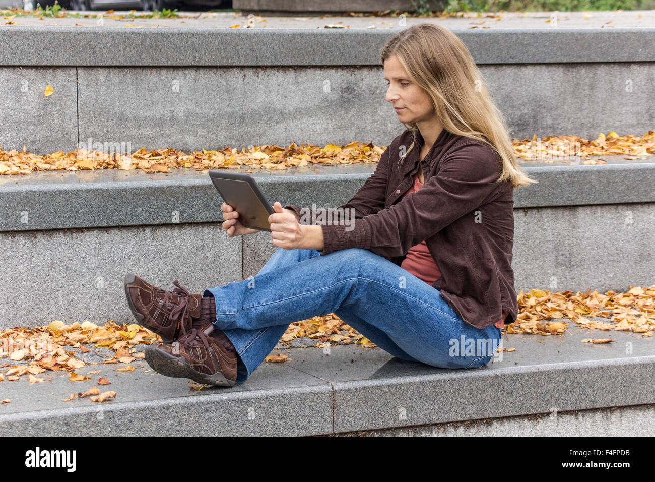 Une femme assise avec un tablet PC un escalier en pierre grise avec des feuilles d'automne jaune Banque D'Images