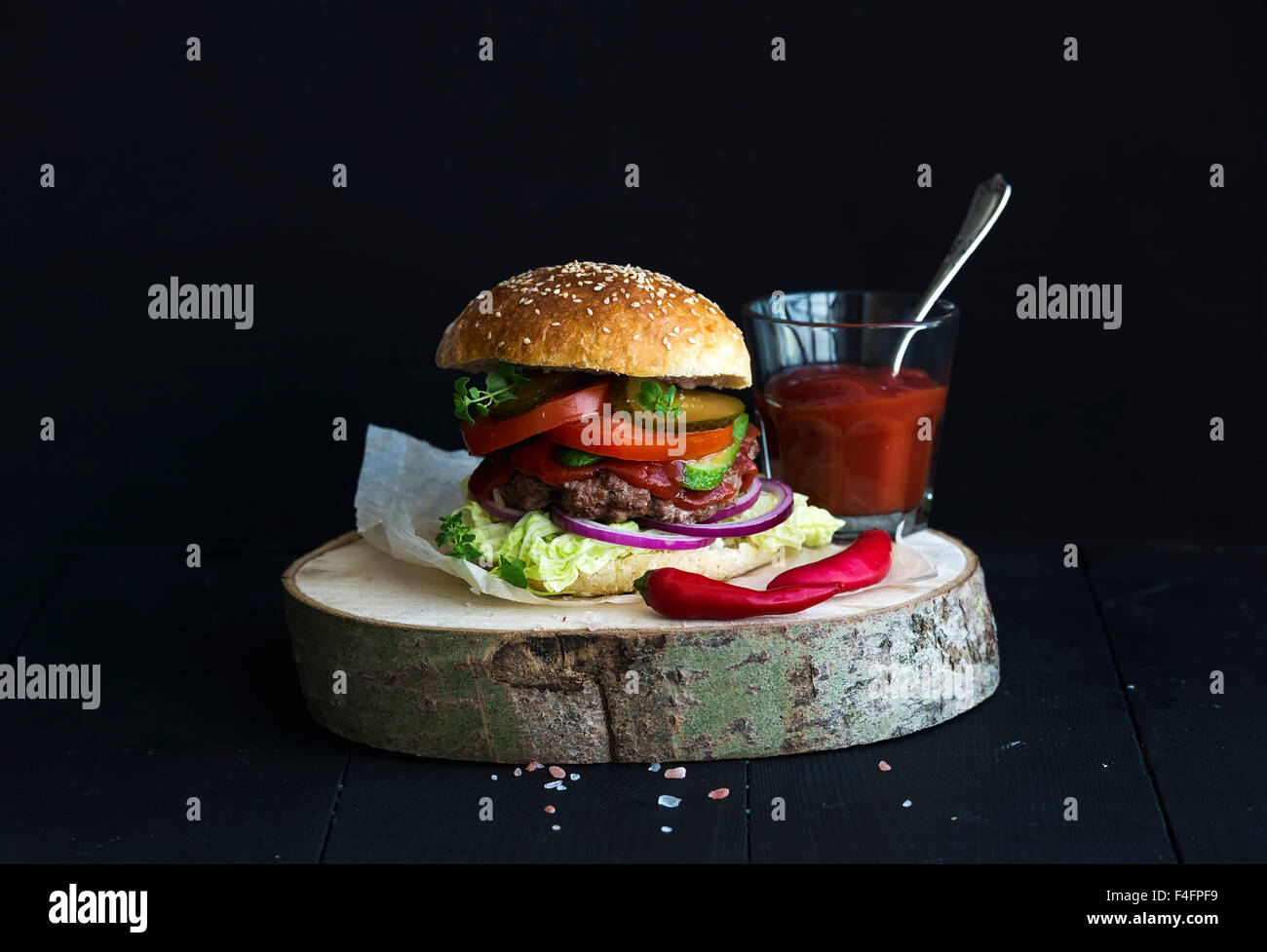 Burger maison en bois servant à bord avec la sauce tomate, sel de mer et herbes sur fond noir Banque D'Images