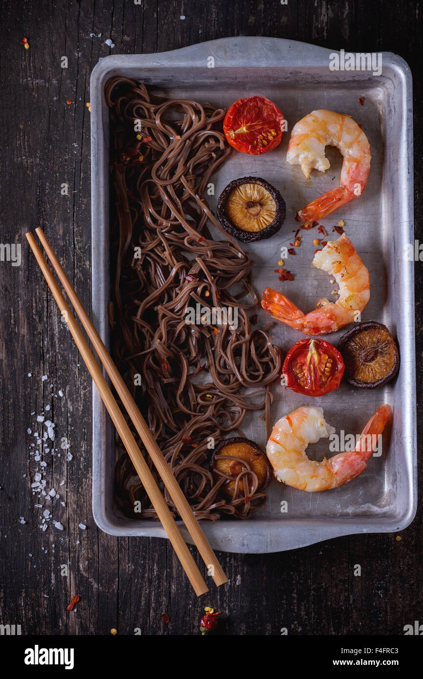 Dîner de style asiatique avec des nouilles soba, des champignons shiitake, des tomates grillées et les crevettes dans un plat de cuisson en aluminium avec les côtelettes en bois Banque D'Images