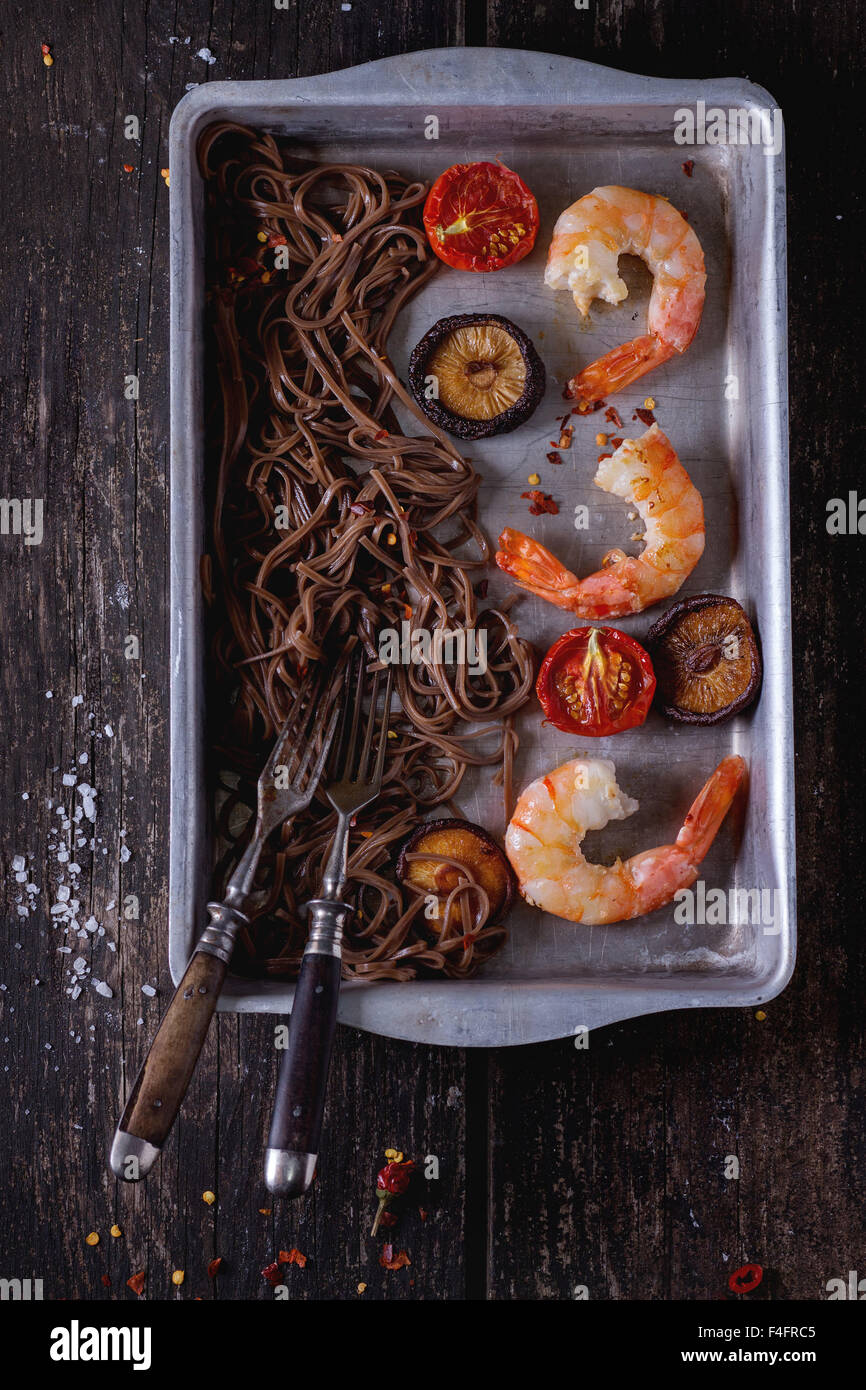 Dîner de style asiatique avec des nouilles soba, des champignons shiitake, des tomates grillées et les crevettes dans un plat de cuisson en aluminium avec fourche vintage Banque D'Images