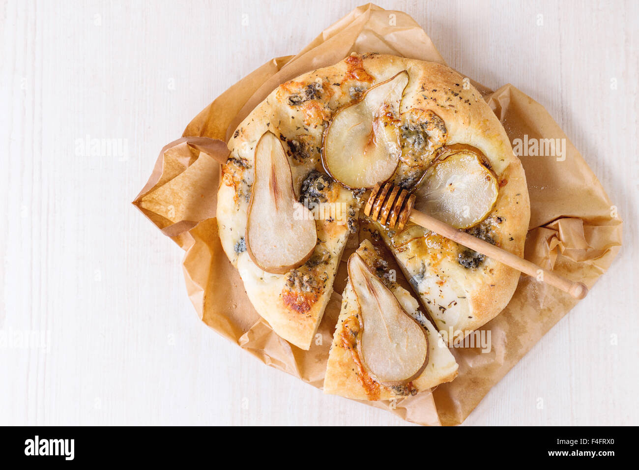 Tranches de Pizza au gorgonzola, poire et miel Miel de bois d'olivier avec balancier sur papier cuisson sur table en bois blanc. Vue d'en haut Banque D'Images