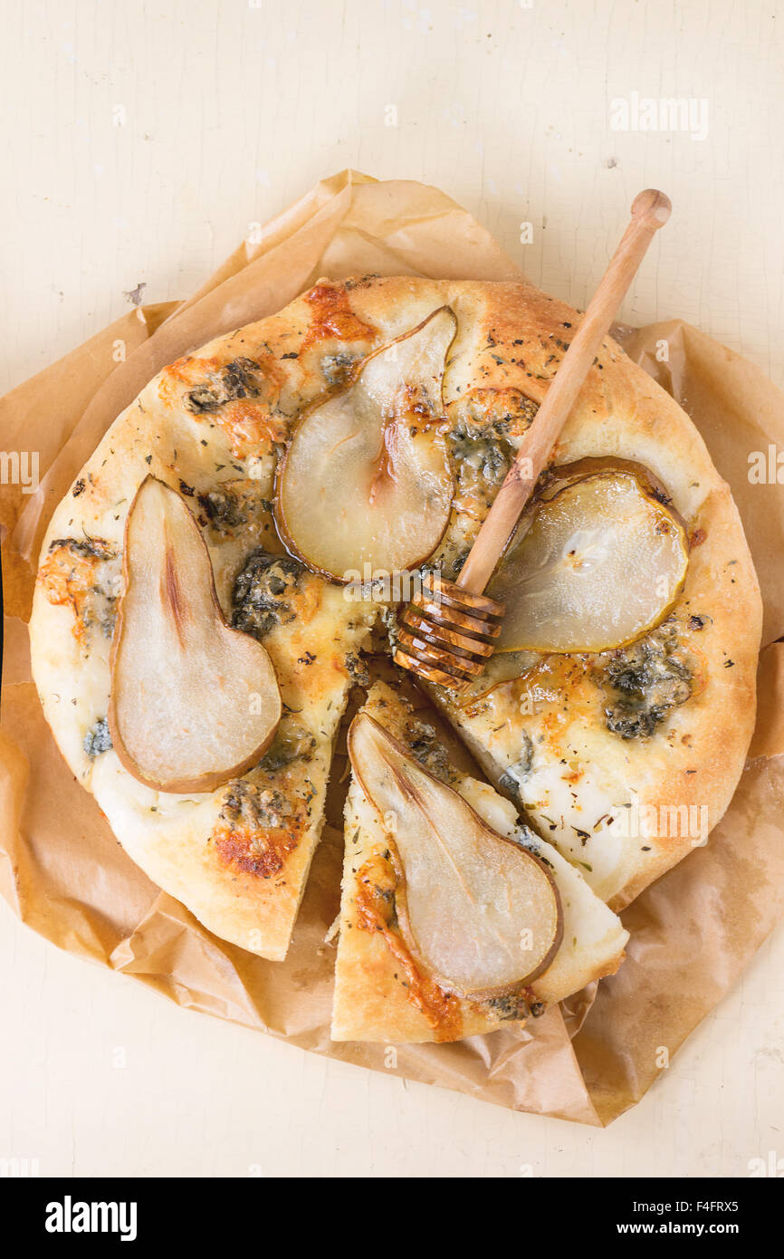 Tranches de Pizza au gorgonzola, poire et miel avec du miel en bois d'olivier balancier sur papier cuisson sur table en bois blanc. Vue d'en haut Banque D'Images