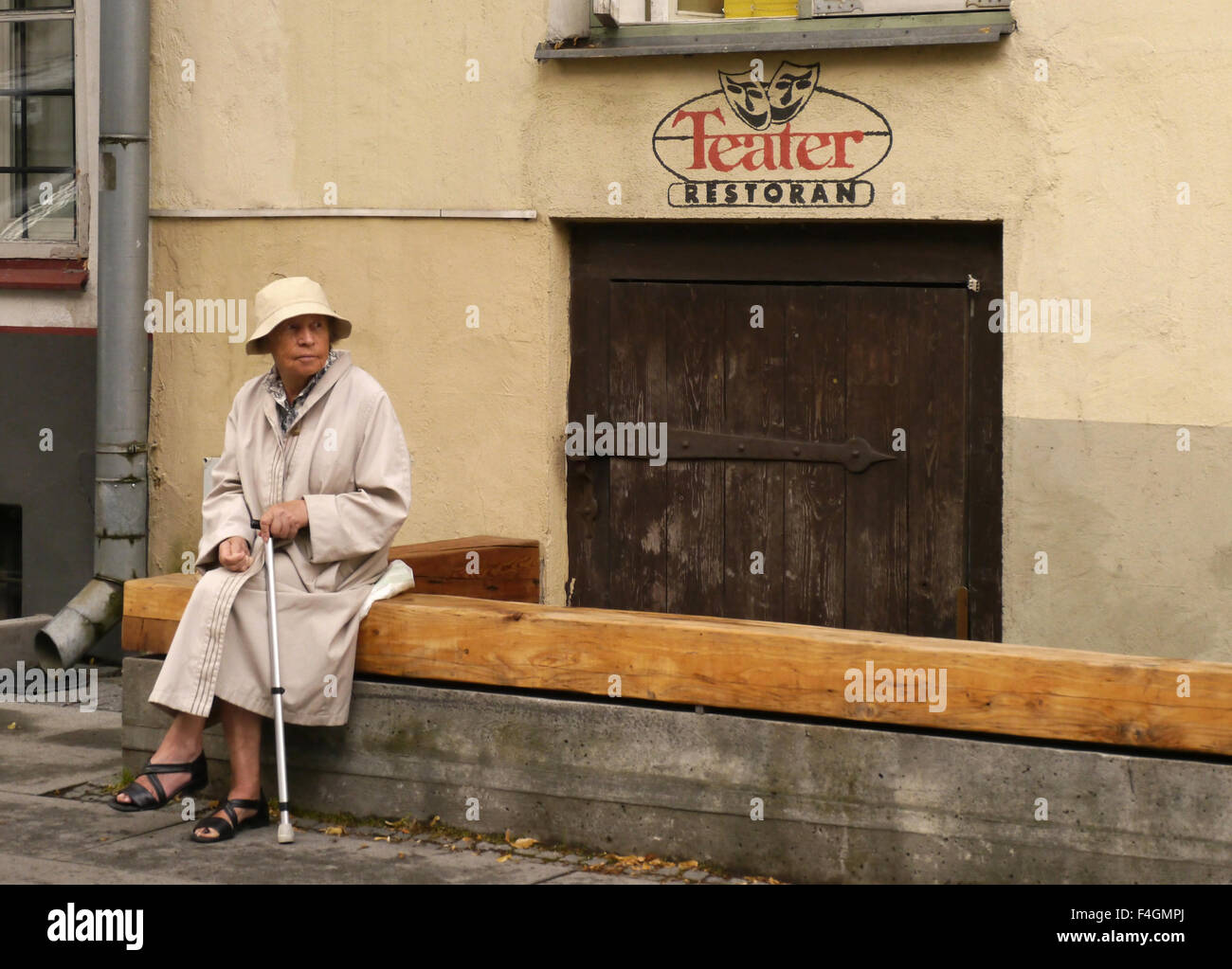 Une vieille femme assise sur un mur avec un bâton de marche à l'extérieur d'un restaurant théâtre abandonné à Tallinn, Estonie Banque D'Images