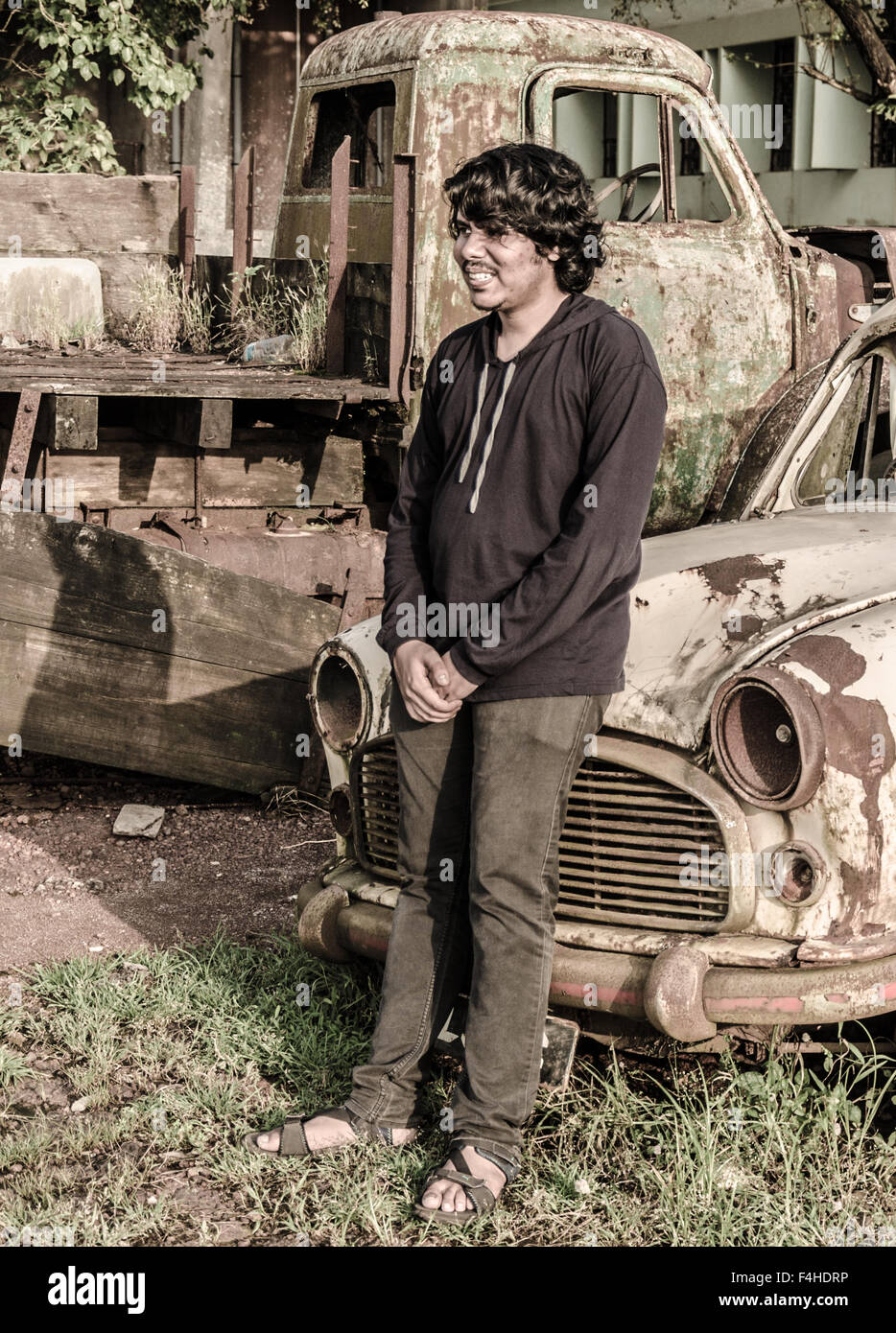 Boy leaning sur le capot d'une vieille voiture rouillée en ferraille. Banque D'Images