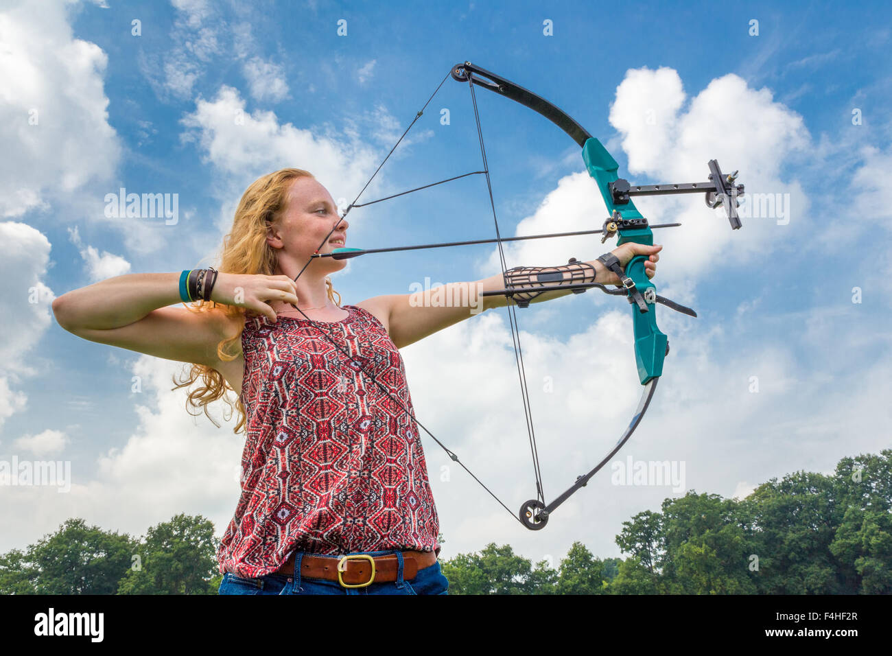 Jeune femme avec Tir Tir à l'arc à poulies contre ciel bleu et nuages blancs Banque D'Images