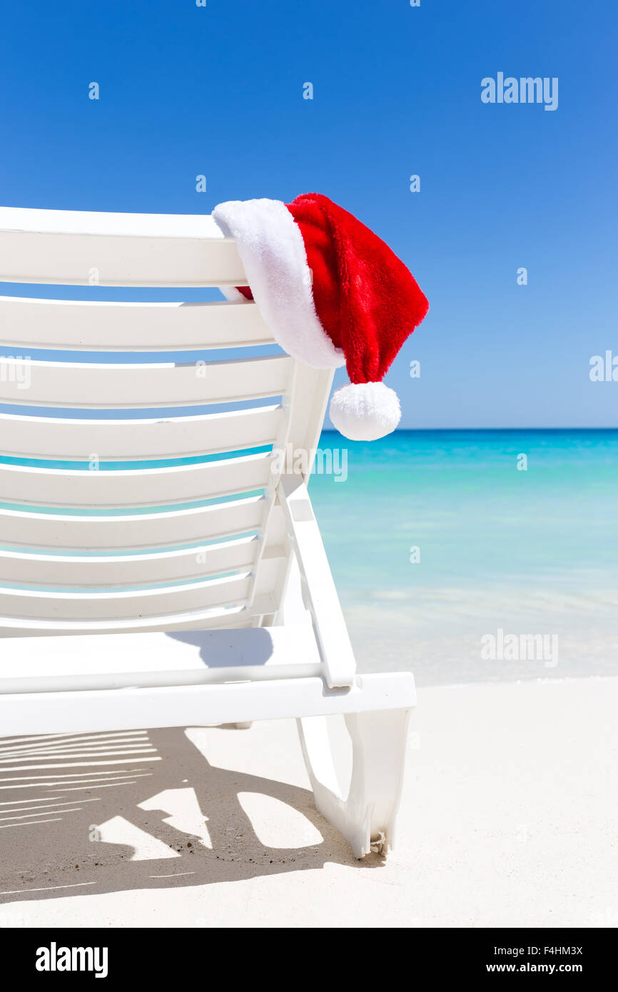 Santa Claus Hat sur les transats près de la plage de sable avec de l'eau de la mer turquoise des Caraïbes. Carte de Noël tropical Banque D'Images