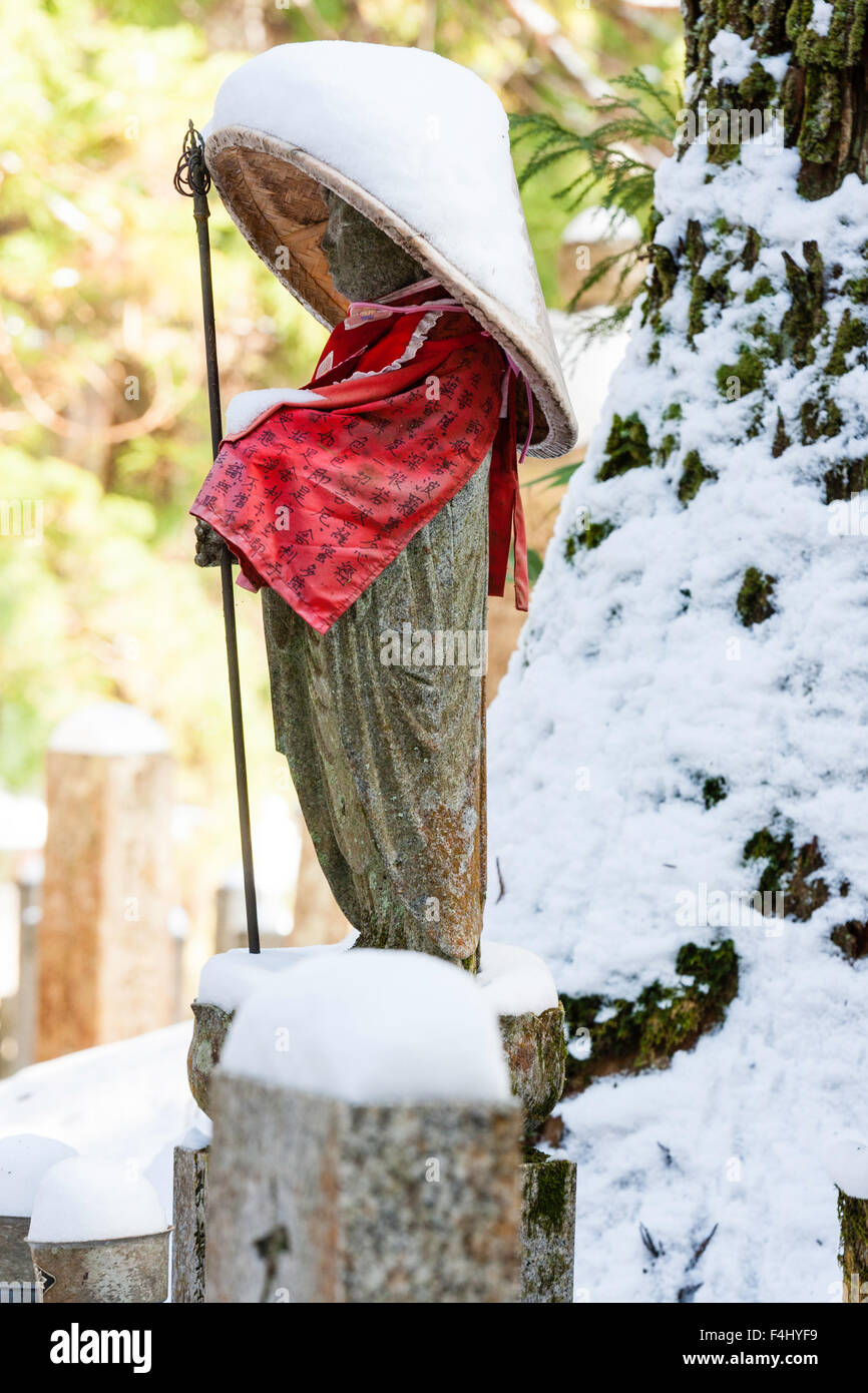 Le Japon, Koyasan, Okunoin cemetery. Prêtre de la pierre couverte de neige rouge statue bouddhique, soumission et chapeau conique, et la tenue du personnel. L'hiver Banque D'Images