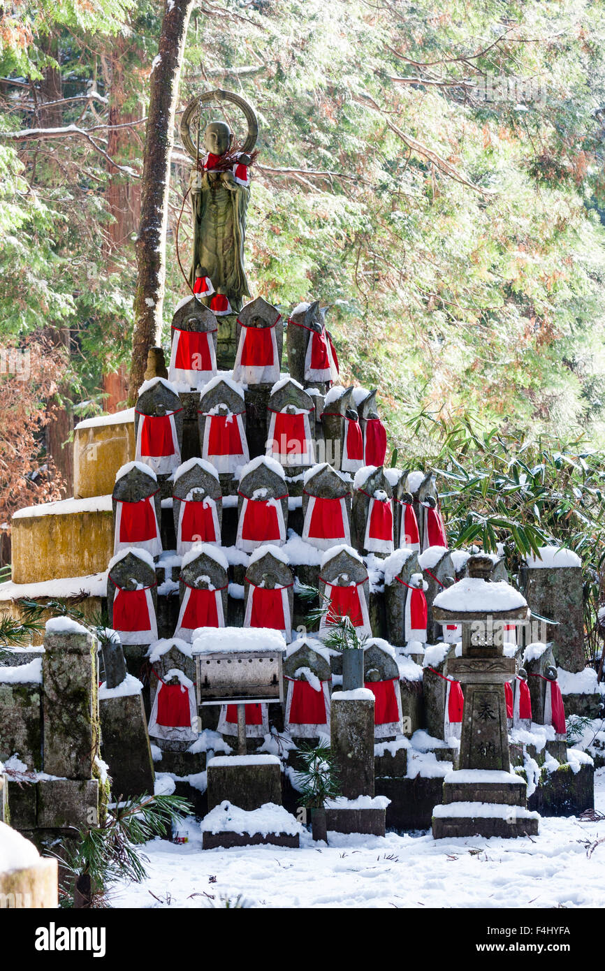 Le Japon, Koyasan, Okunoin cemetery. La neige a couvert les petits rouges-bibbed statues jizo-bosatsu empilées en pyramide avec grande statue bosatsu sur le dessus. Banque D'Images