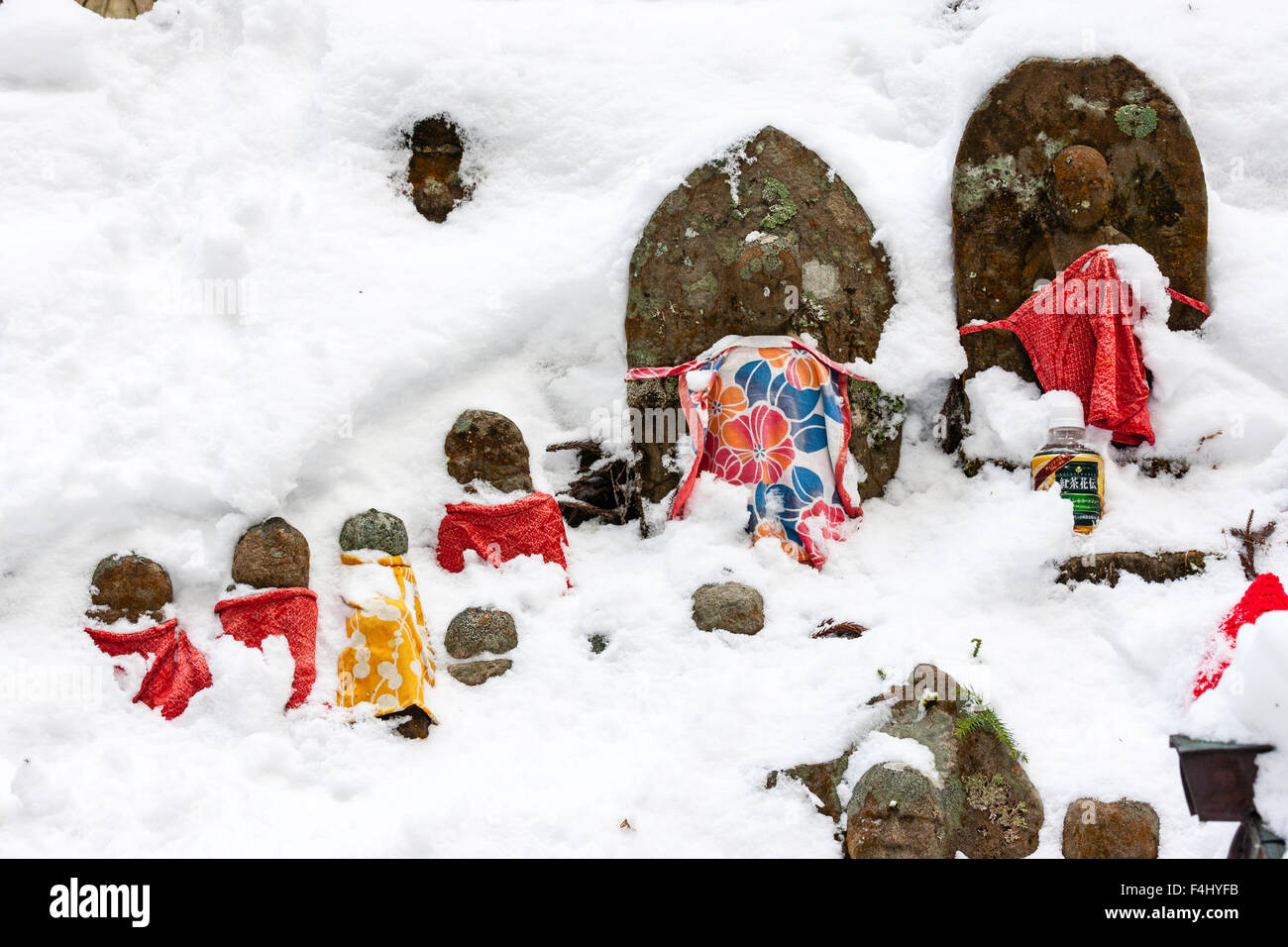 Le Japon, Koyasan, Okunoin cemetery. Rangée de petites à grandes tailles jizo bosatsu bibbed rouge-statues à demi couvert d'une épaisse couche de neige au sol. Banque D'Images