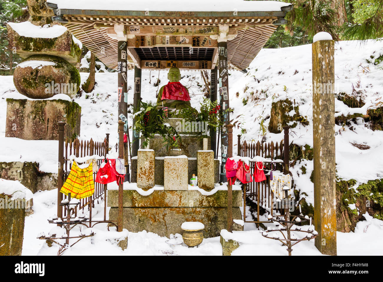 Koyasan, Japon, cimetière Okunoin, la plus grande du Japon. La neige a couvert de culte tombe avec red bibbed statue Jizo Bosatsu sous petit toit en bois. Banque D'Images