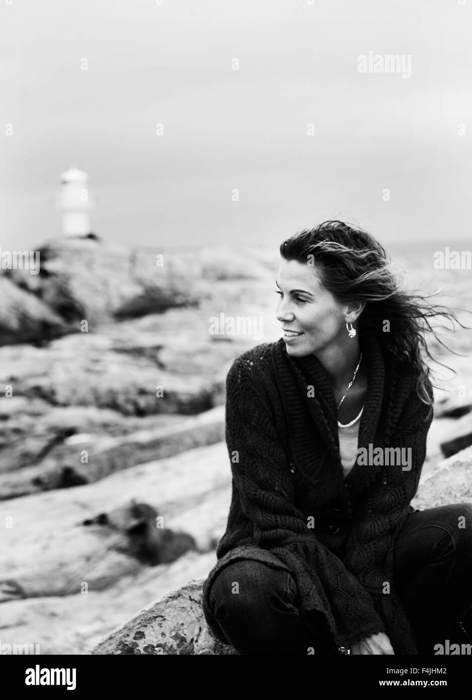 La Suède, Vastkusten, Marstrand, jeune femme assise sur des rochers, phare dans la distance Banque D'Images