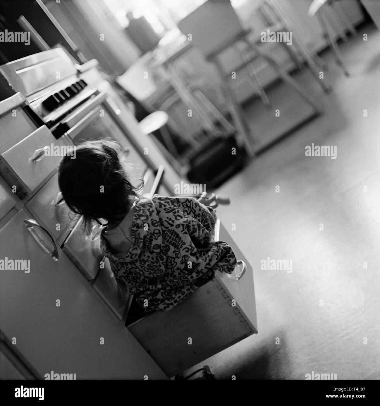 Fille assise à l'intérieur de tiroir dans la cuisine, vue arrière Banque D'Images