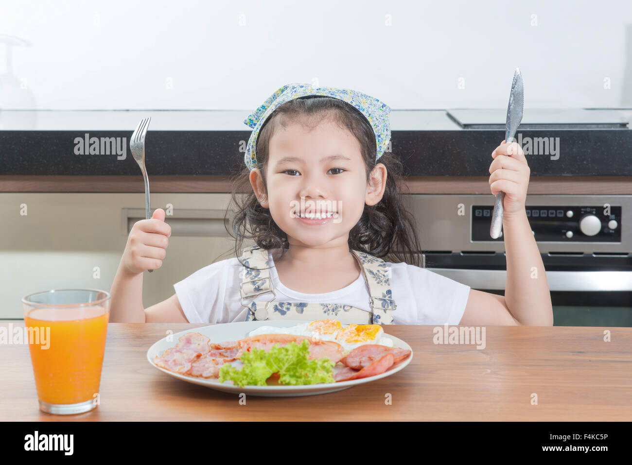 La famille, les enfants et les gens heureux concept - Asian girl enfant de manger le petit déjeuner américain à l'accueil Banque D'Images
