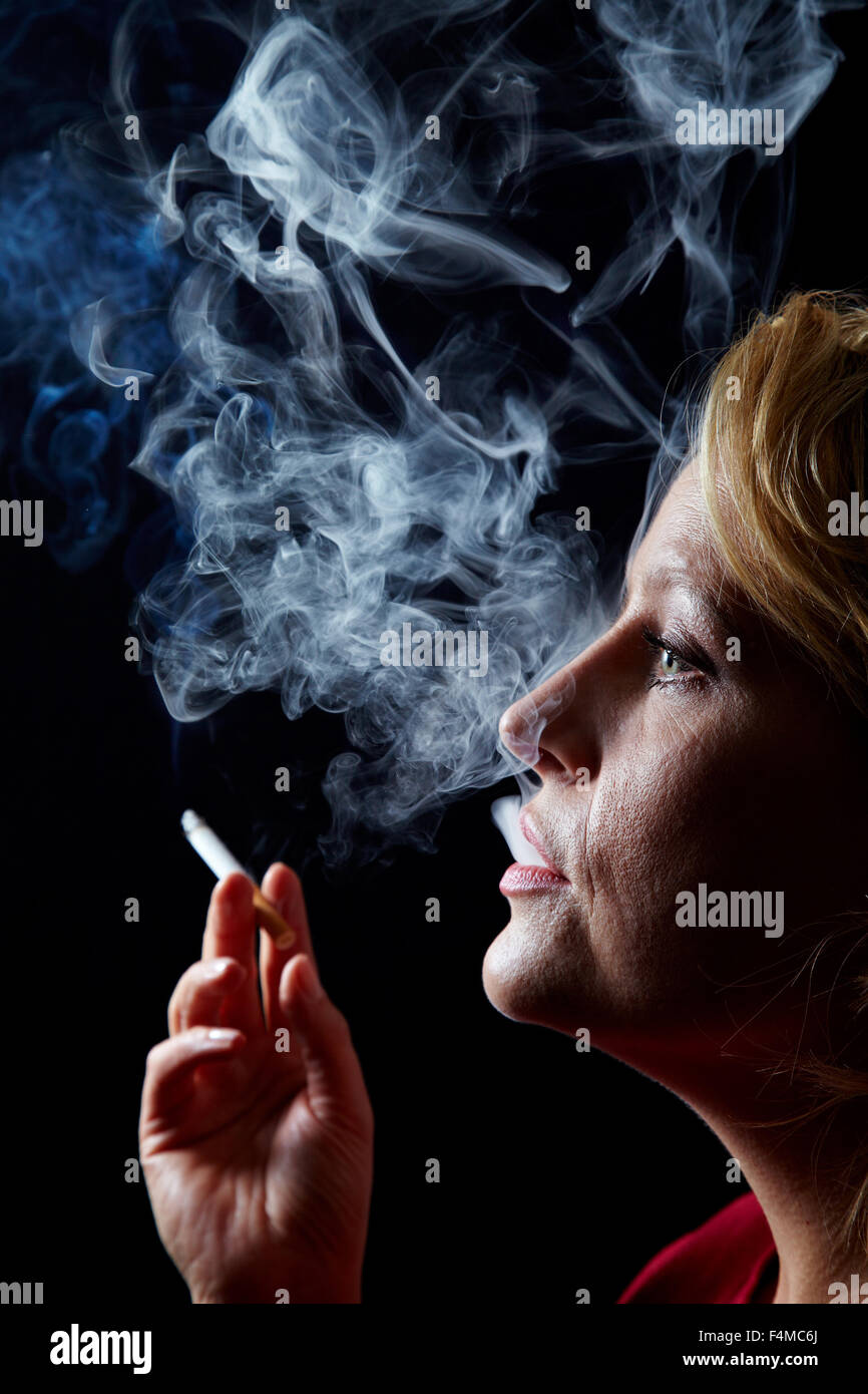 Femme exhalant la fumée de cigarette sur fond noir Banque D'Images