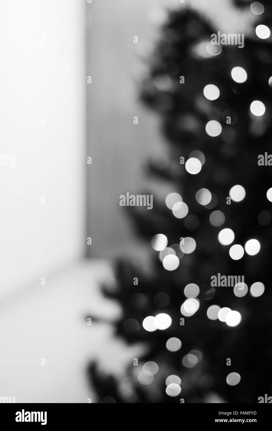 Un noir et blanc vertical arrière-plan flou créé par un ensemble de feux de flou artistique sur un côté d'un arbre de Noël. Banque D'Images