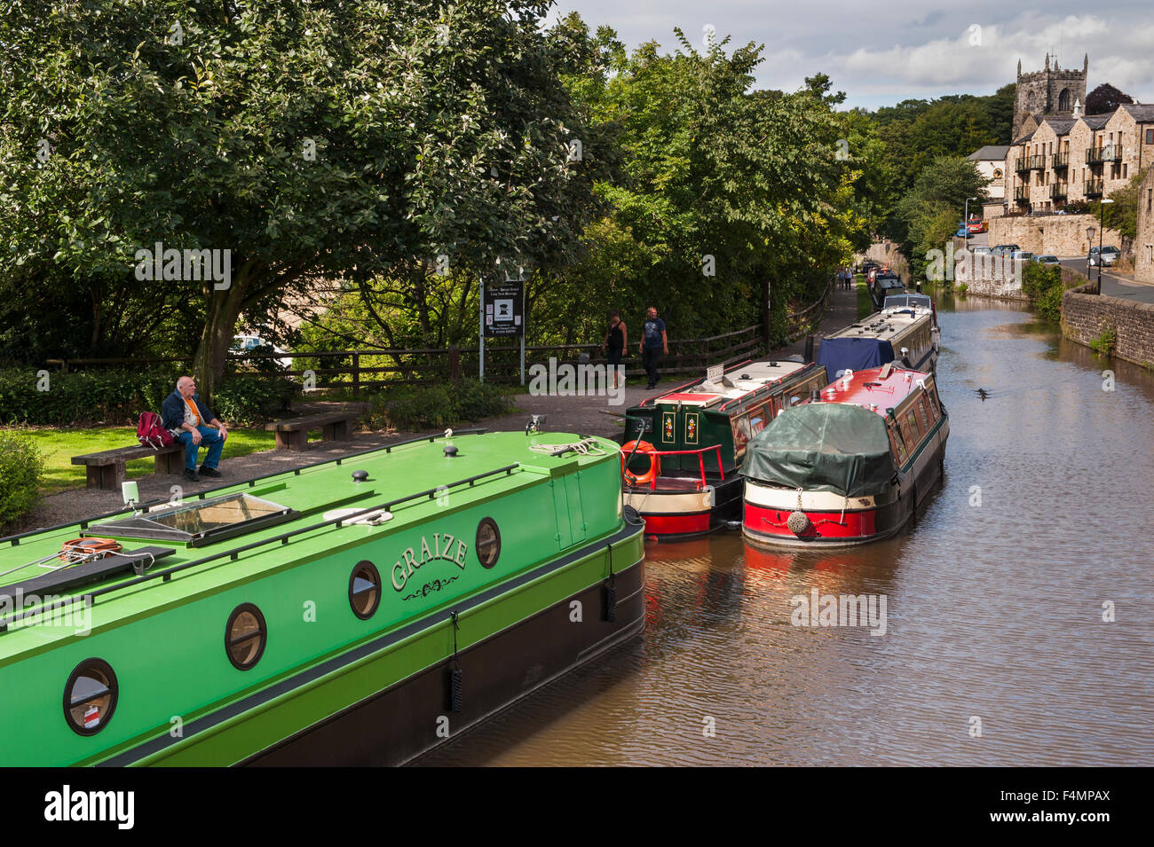 L'été ensoleillé, vue sur le canal bateaux amarrés et les gens se détendre sur chemin de halage - Ressorts, Direction générale du canal Leeds-Liverpool, Skipton, Yorkshire, Angleterre. Banque D'Images