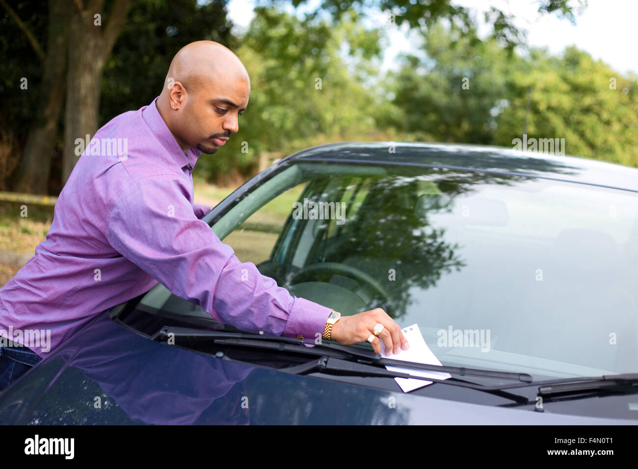 Jeune homme de laisser un message sur un pare-brise de voiture Banque D'Images