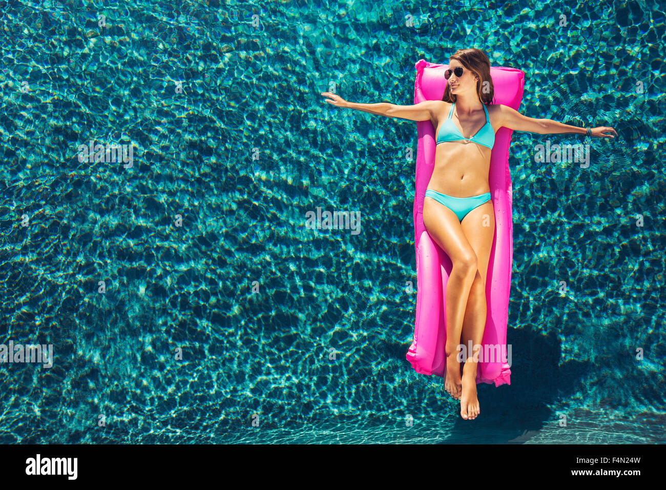 Belle jeune femme flottant relaxant sur radeau dans piscine de luxe Banque D'Images