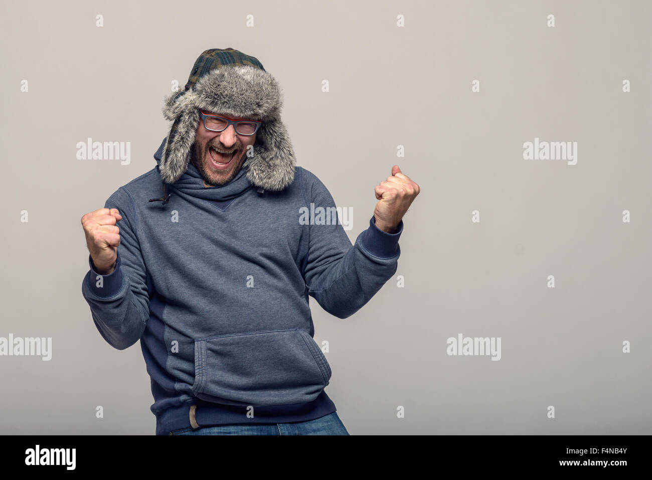 Heureux homme portant des lunettes et un chapeau d'hiver de clameurs et de célébrer son poings serrés dans l'air avec une exaltante expre Banque D'Images