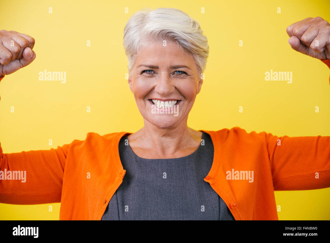 Portrait of young woman standing comme superwoman en face d'un mur jaune Banque D'Images