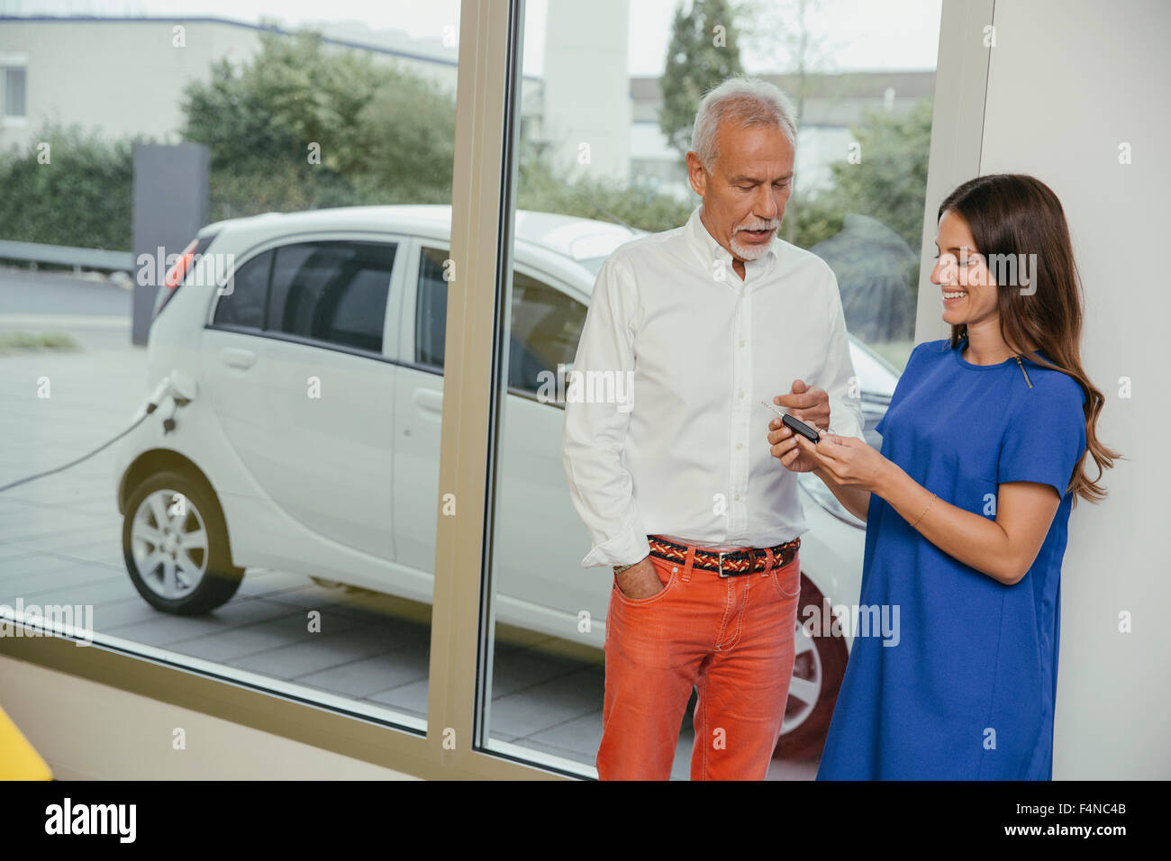 L'homme et de la femme de parler pendant la recharge de la voiture électrique, woman holding key Banque D'Images