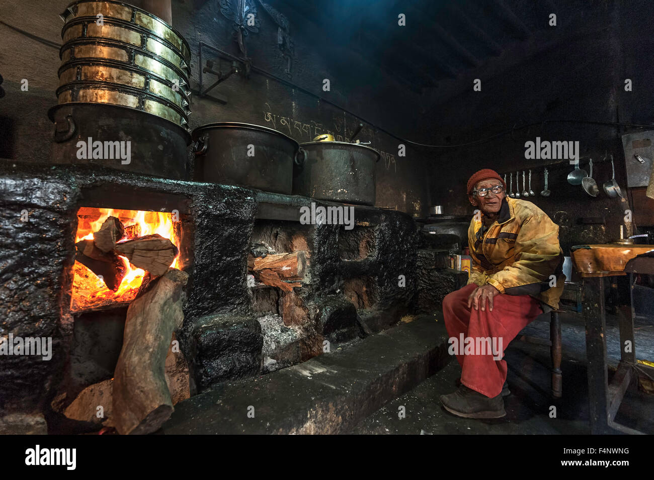 Vieux moine est assis dans la cuisine à côté de l'incendie. Banque D'Images